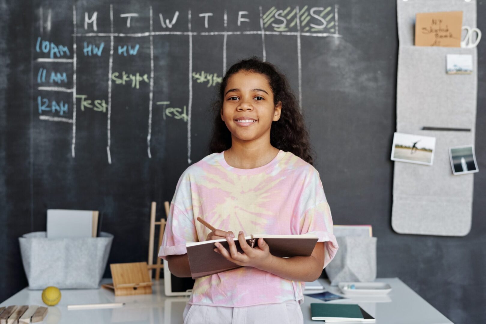 A girl holding a notebook in front of a chalkboard.